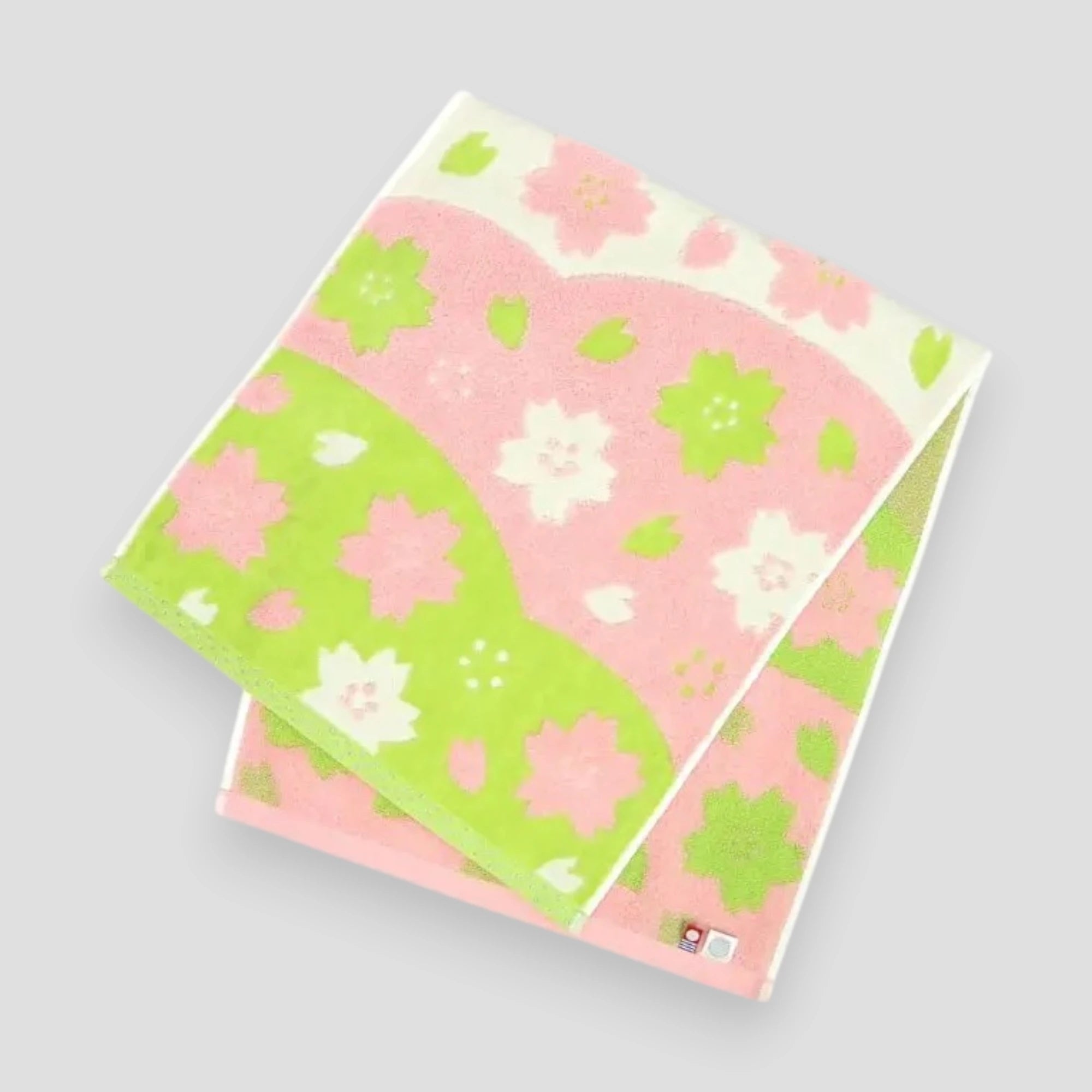 Folded cotton Imabari towel with a floral jacquard pattern in pink, white, and green colors.