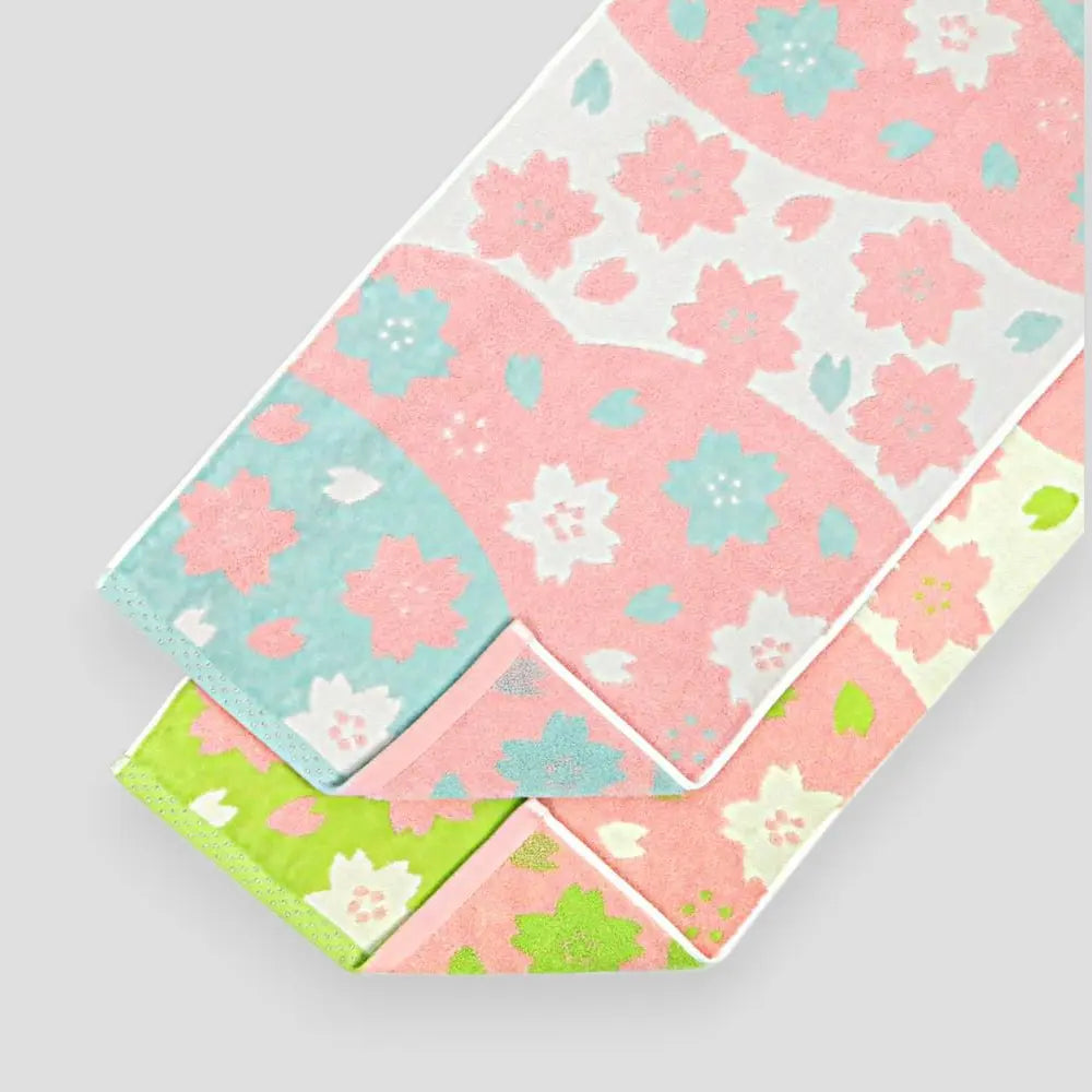 A set of folded cotton towels with a floral jacquard pattern in pink, white, and green colors.