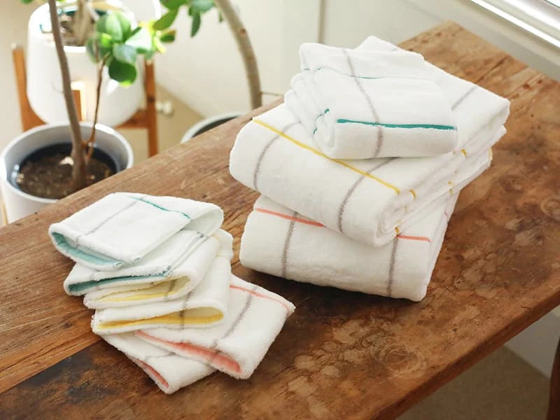 A set of white Imabari towels with multicolored stripes, displayed on a wooden surface.