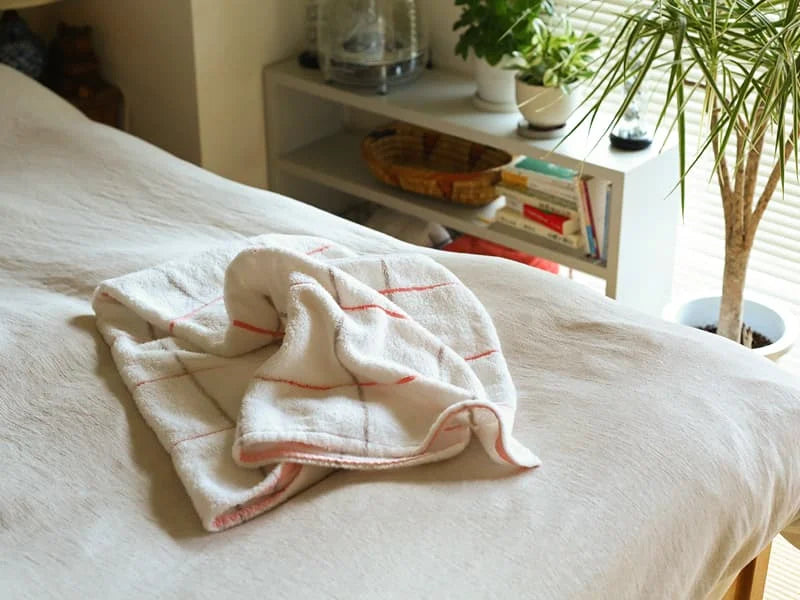Folded white Imabari towel with pink and gray line on the bed