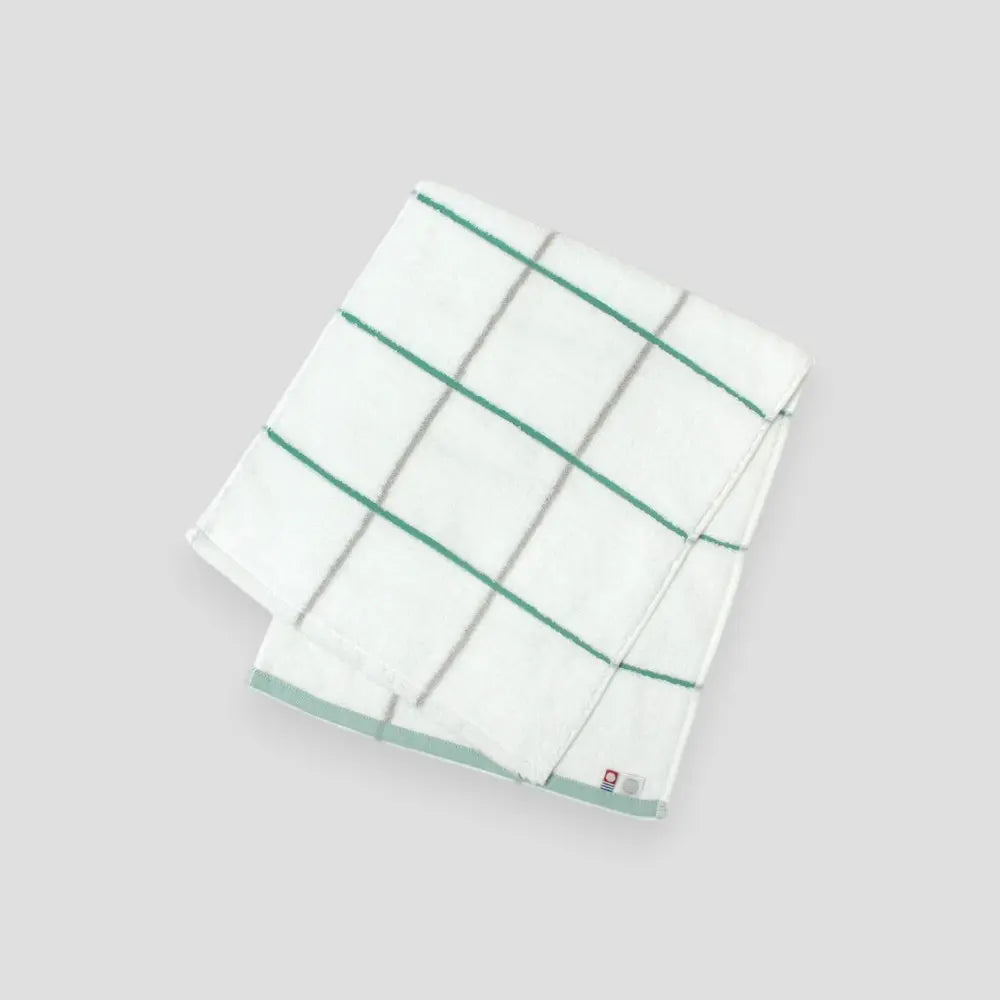 Folded white Imabari towel with green stripes on a light gray background