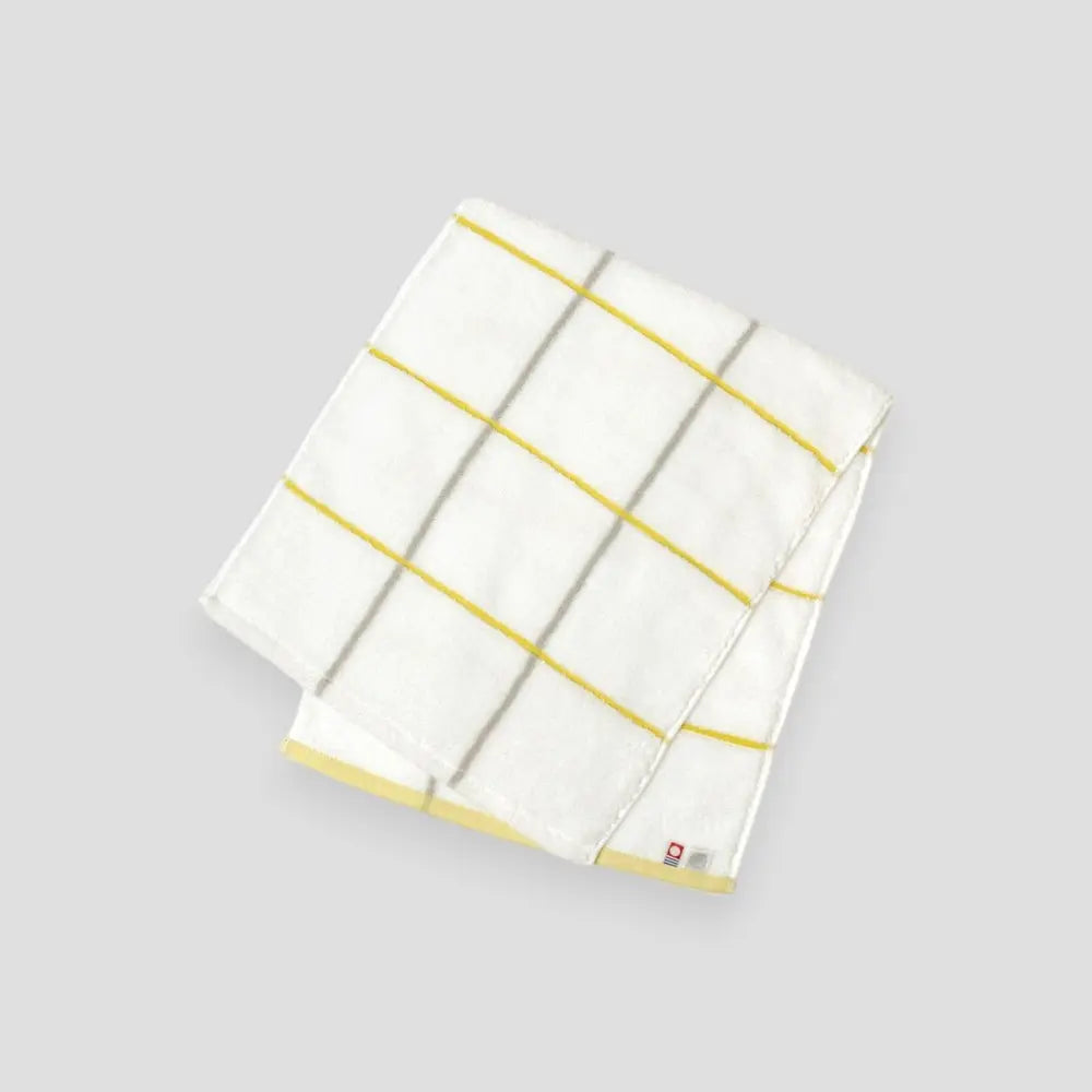 Folded white Imabari towel with yellow stripes on a light gray background