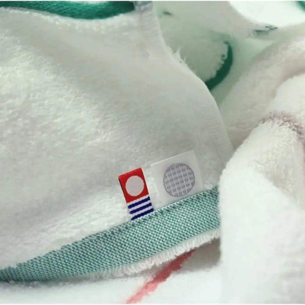 Close-up of white Imabari towel with green  and gray line with labels of Imabari brand mark and IORI brand logo.
