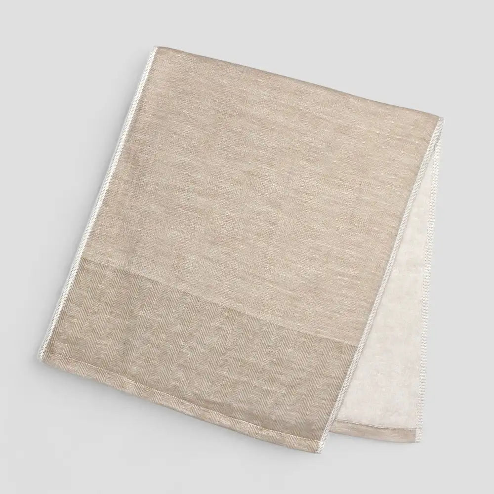 Folded beige Imabari towel with a subtle herringbone pattern on a light gray background.