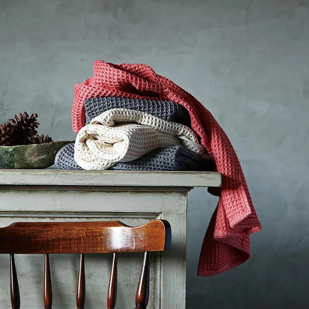 Stack of three folded Imabari towels in red, navy, and beige on a light gray background