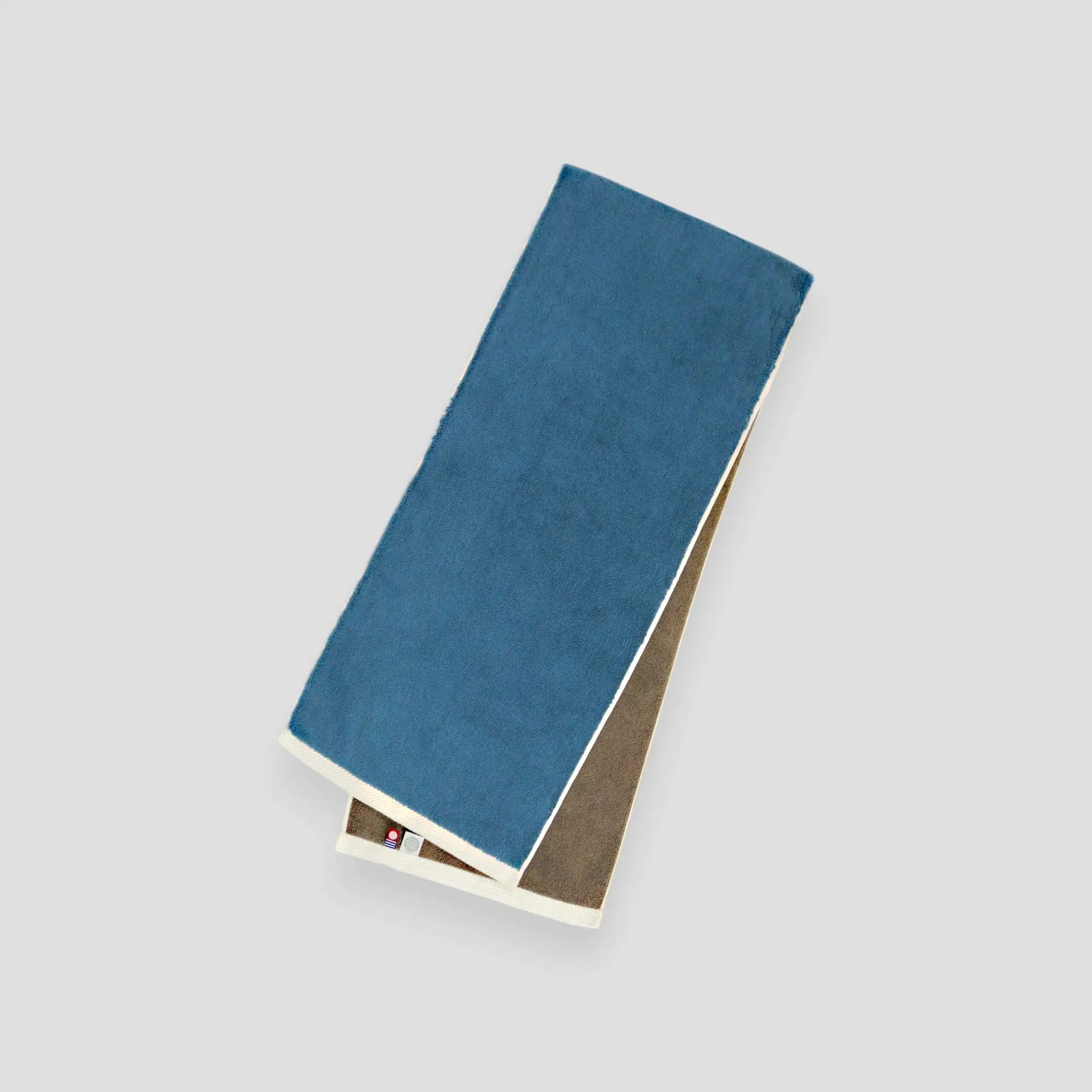 A folded blue and gray reversible Imabari towel with the brand label visible