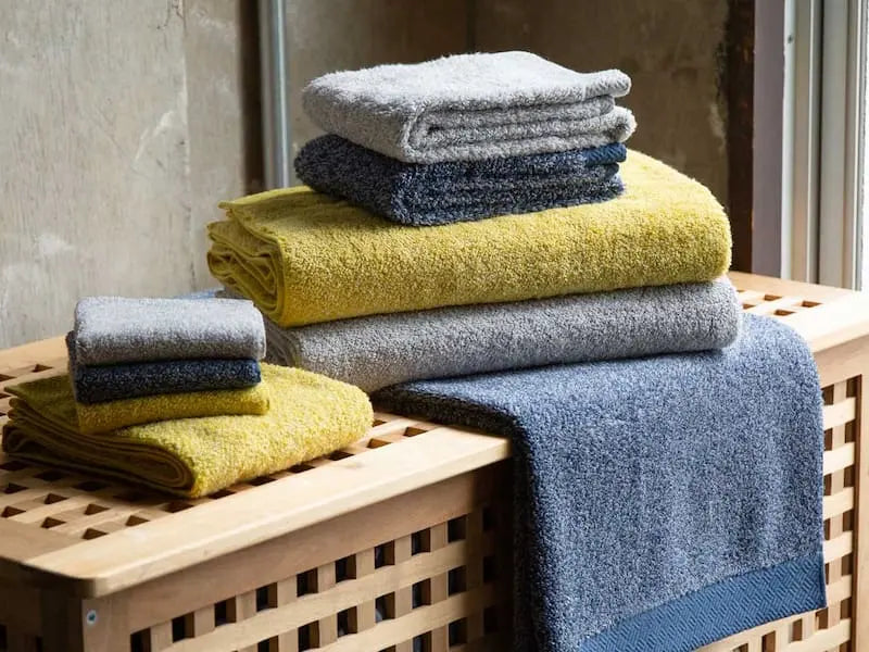 Stack of folded Imabari towels in yellow, gray, and navy colors on a wooden table.