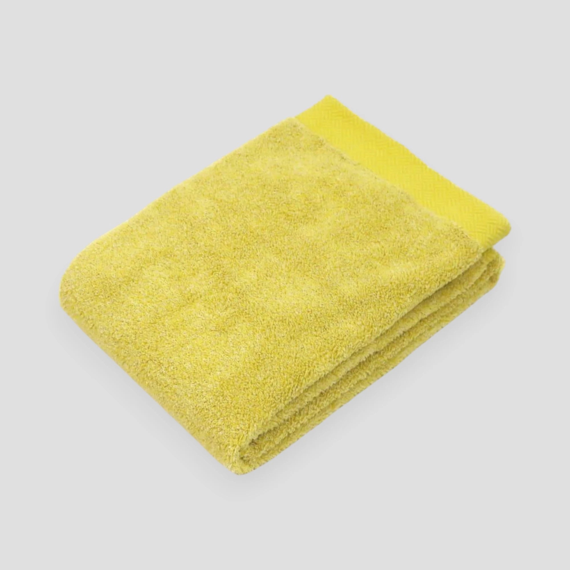 Folded yellow Imabari towel with light gray background.