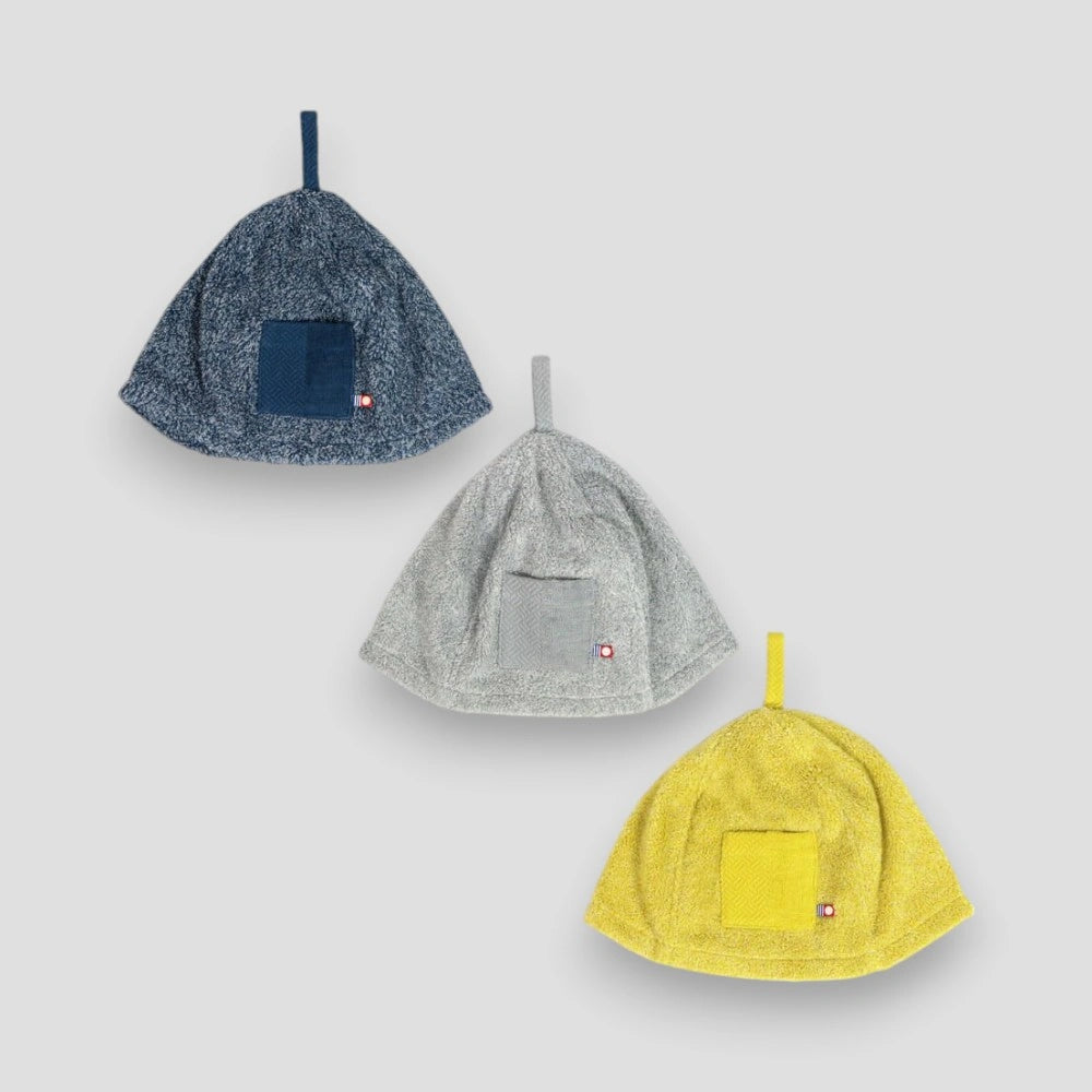 Three KASUMI sauna hats made from Imabari towel in navy, gray, and yellow, each with a different color and a brand tag visible.