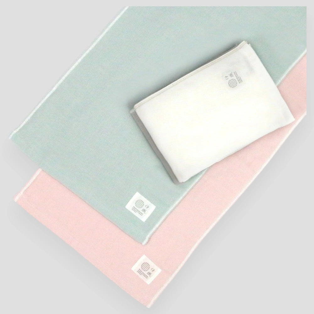 Stack of folded Imabari towels in white, gray, pink, and blue colors made from cotton gauze, branded with a label showing the name &