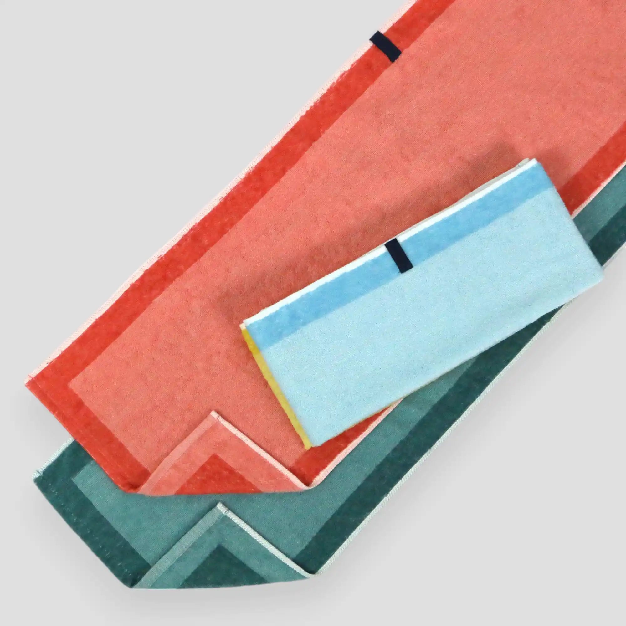 A collection of multi-purpose Imabari towels in various solid colors including, blue, green, and orange, featuring a simple two-tone border design and a hanging loop.