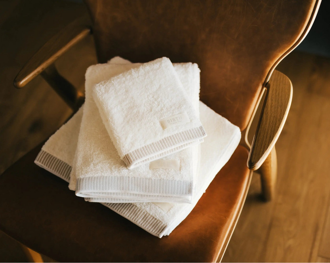 A stack of three folded white towels with ribbed edges resting on a brown leather chair over a wooden floor.
