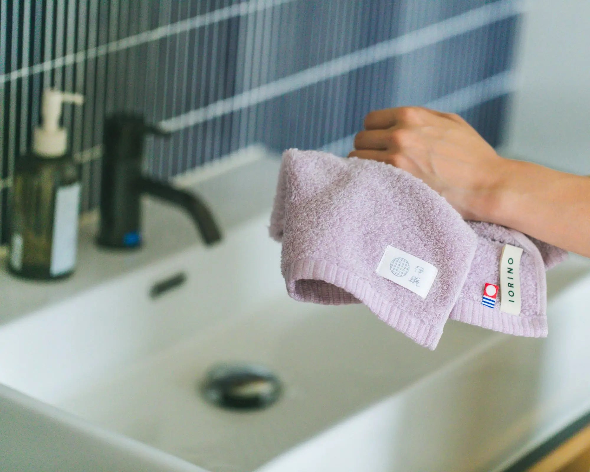 Person holding a purple Imabari towel with a brand label over a sink