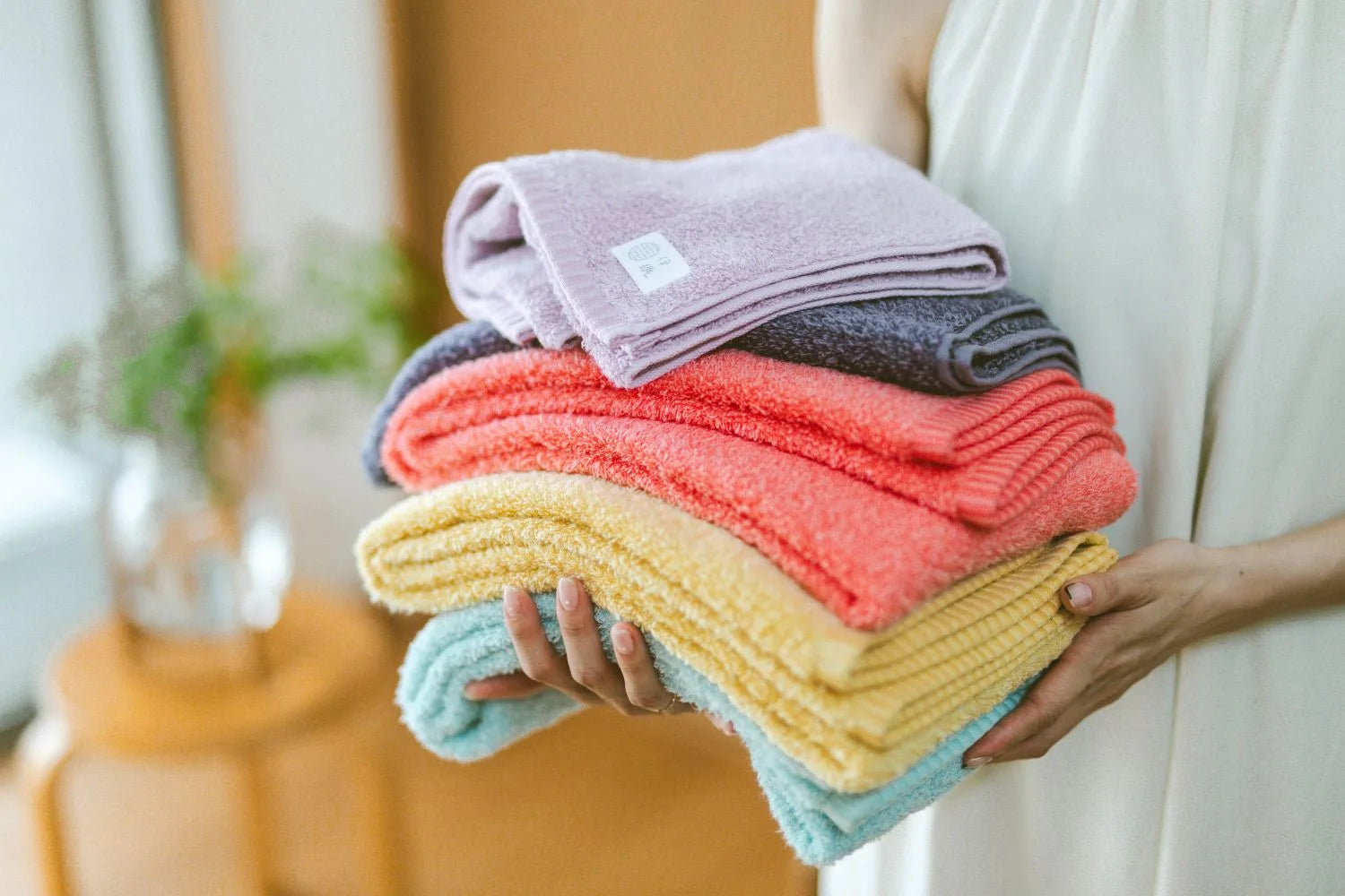 Person holding a stack of colorful folded Imabari towels in a home setting