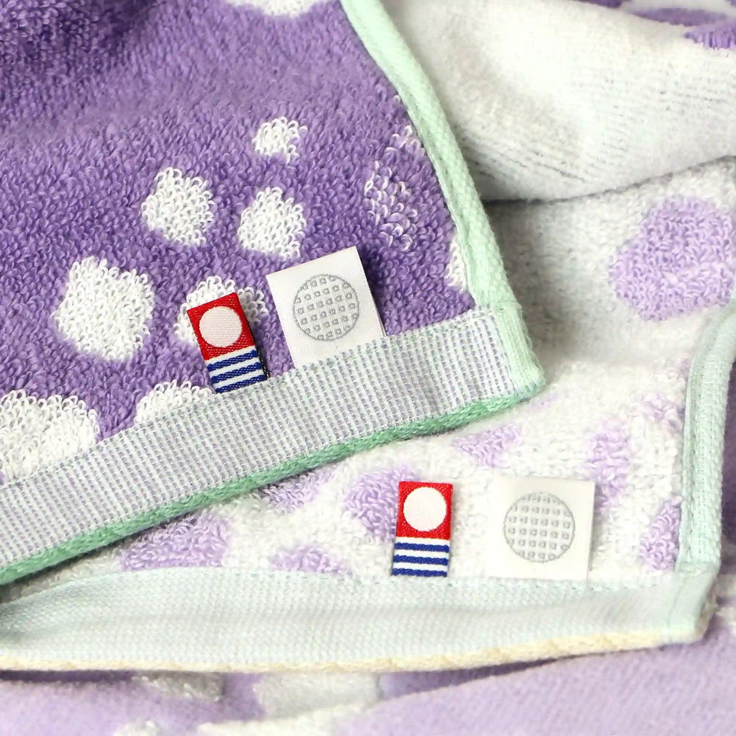 Purple Imabari towel with white floral patterns and small fabric brand tags on a matching background