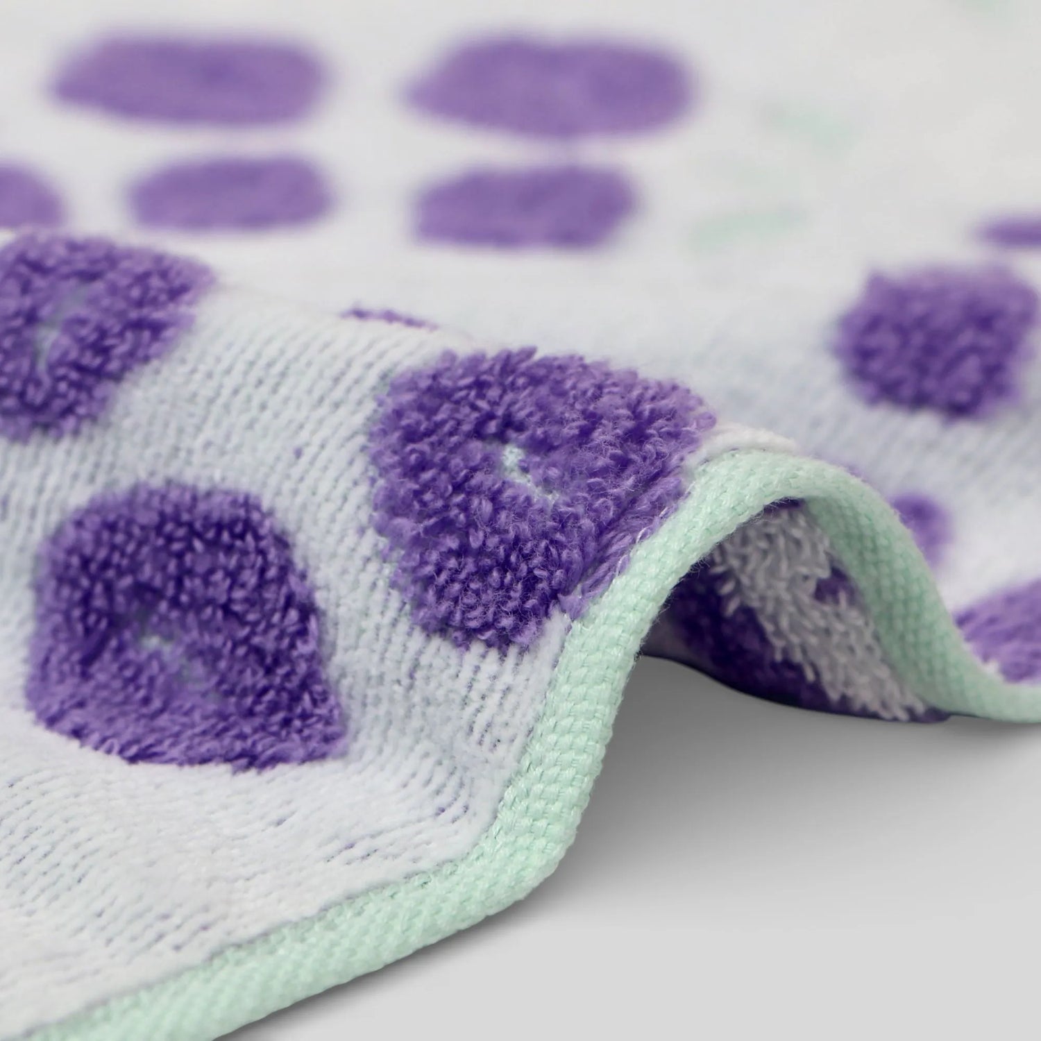 Close-up of a textured fabric with purple and green Iambari towel patterns on a white background