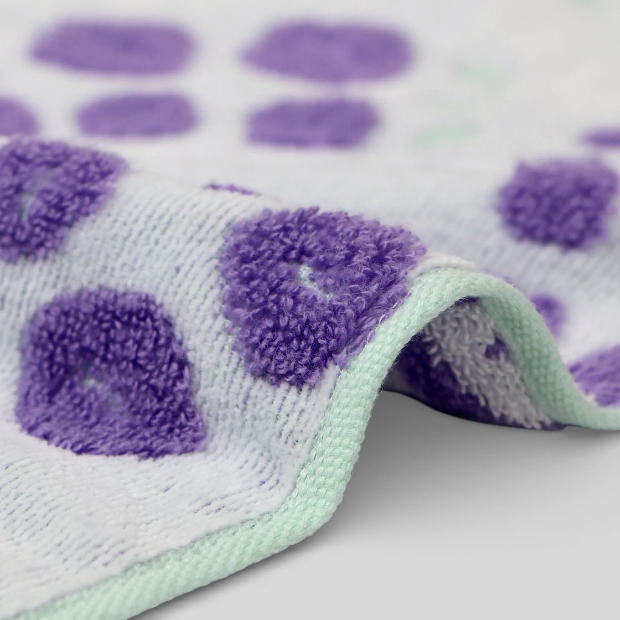 Close-up of a textured fabric with purple and green Iambari towel patterns on a white background