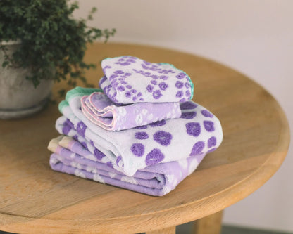 Stack of folded Imabari towels with purple paw print pattern on a wooden table.