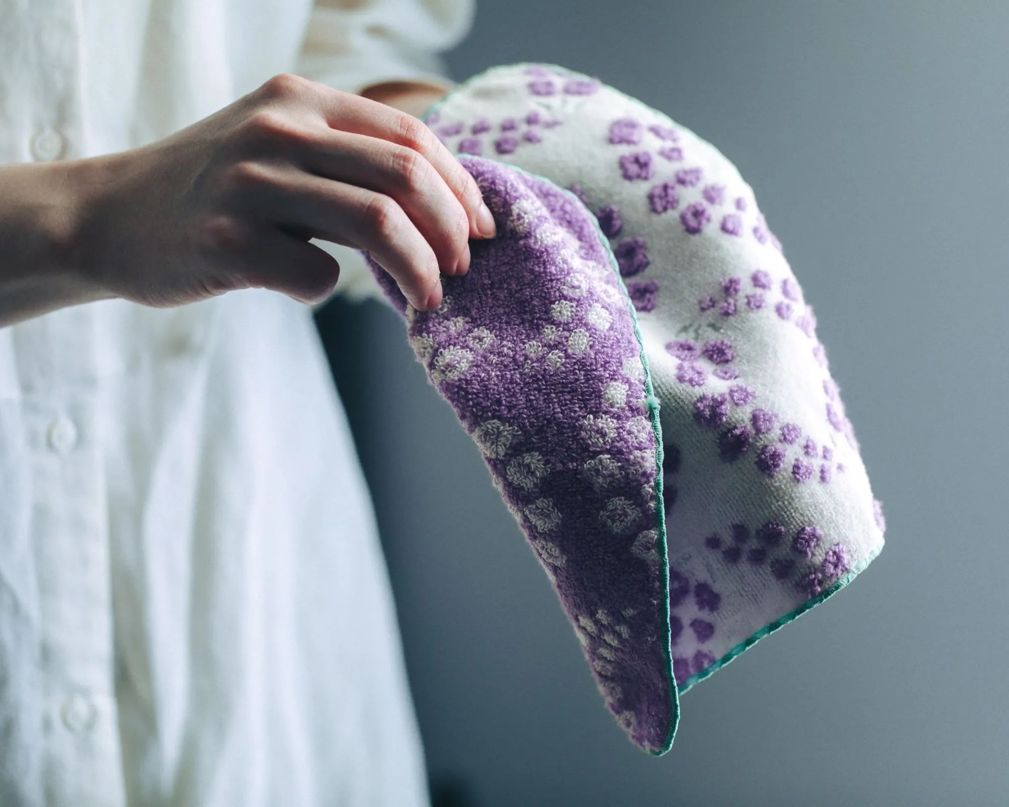 Hand holding a purple and white patterned Imabari towel against a blurred background