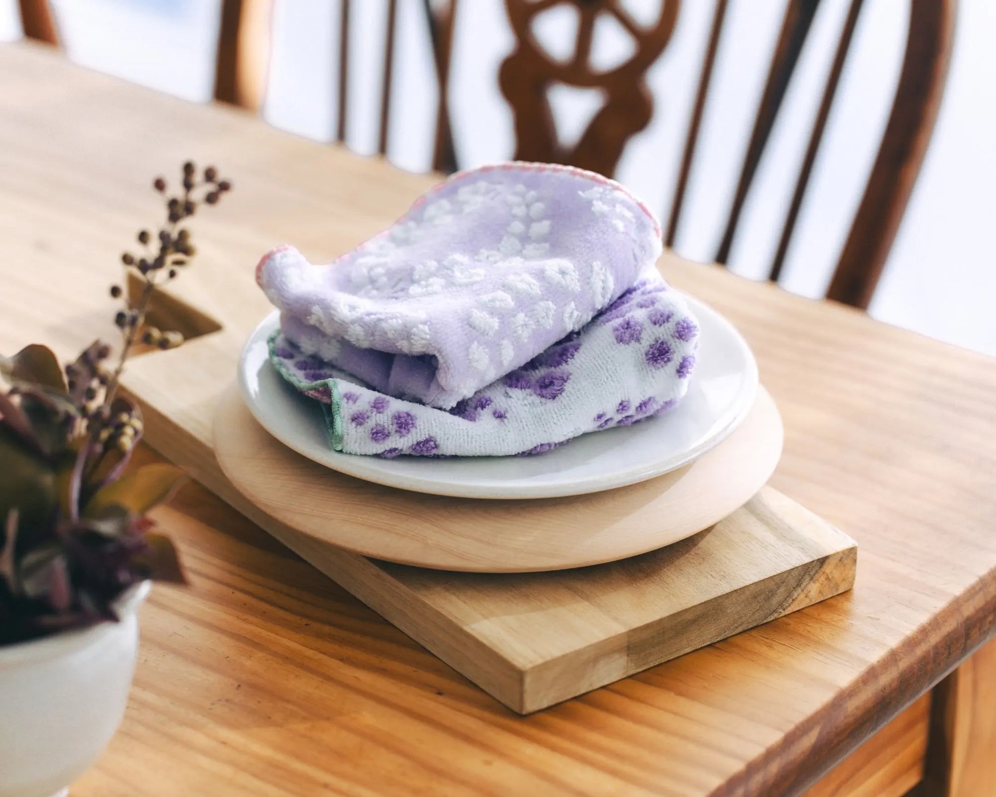 Stack of folded purple and white Imabari towel on a white plate on a wooden table.