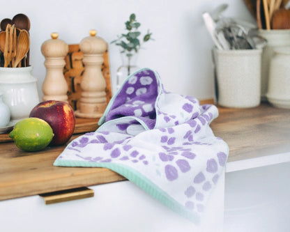 Purple and white patterned Imabari towel on a kitchen counter with utensils and fruits in the background