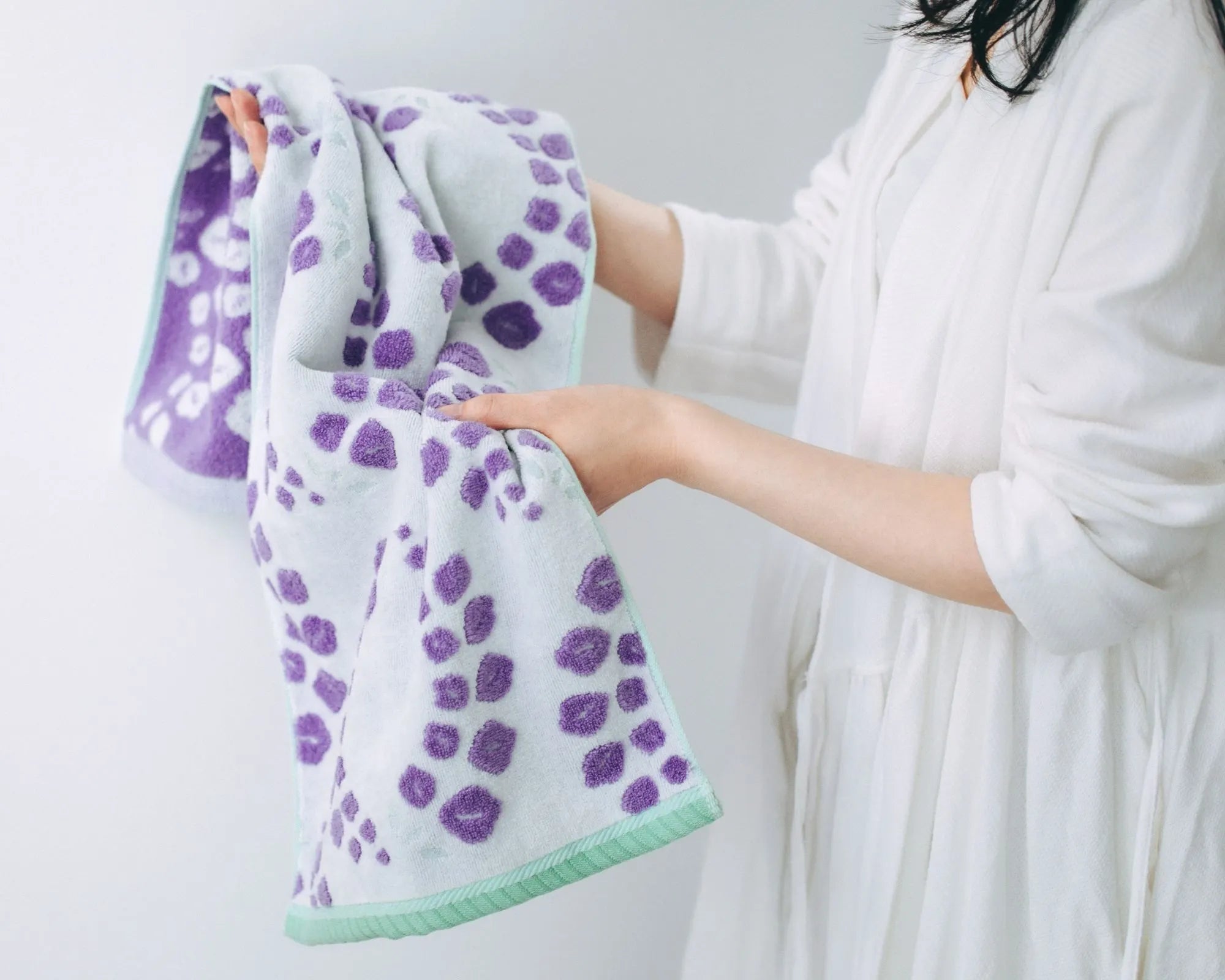 Person holding a Imabari towel with purple floral pattern against a white background