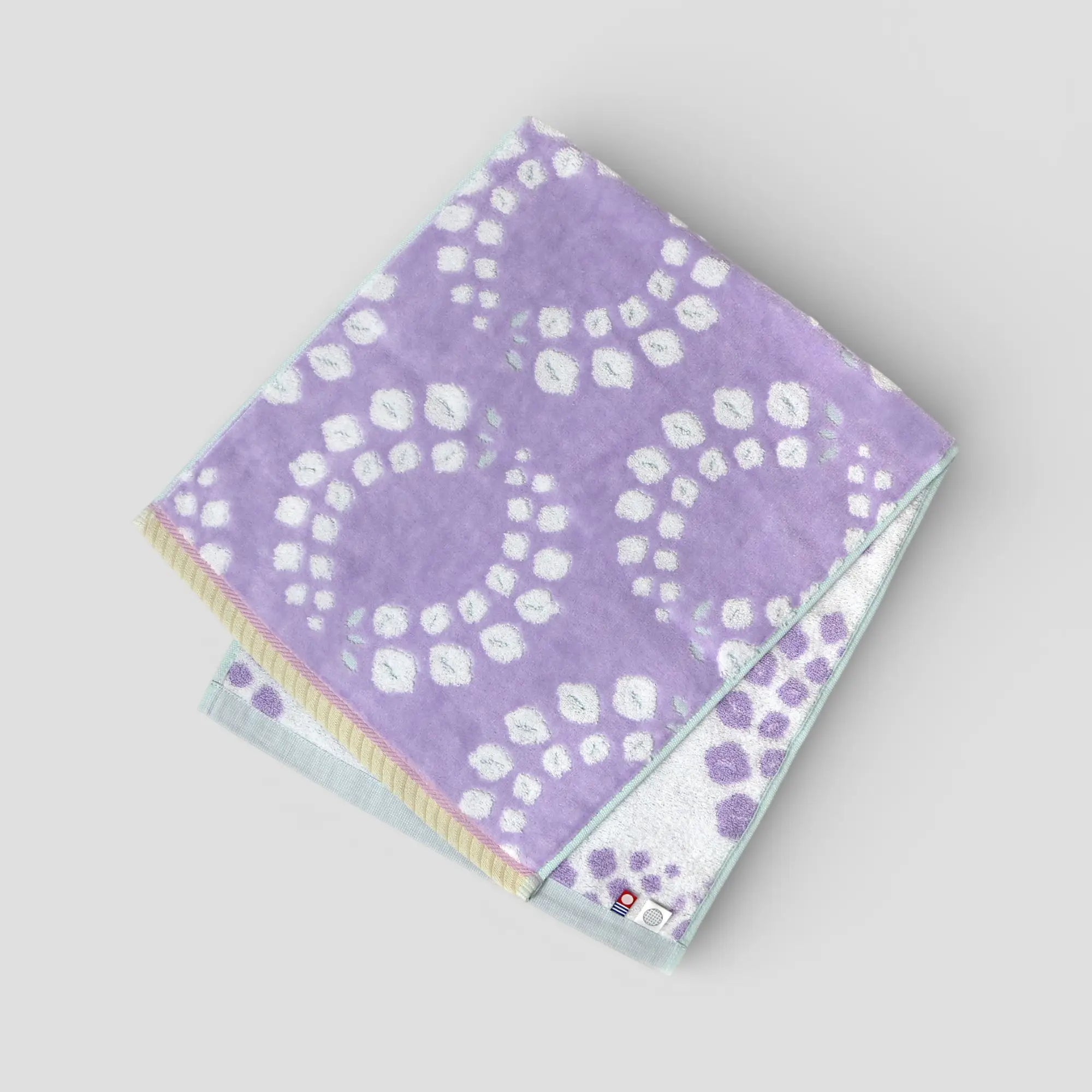 Folded purple Imabari towel with white floral pattern on a light gray background