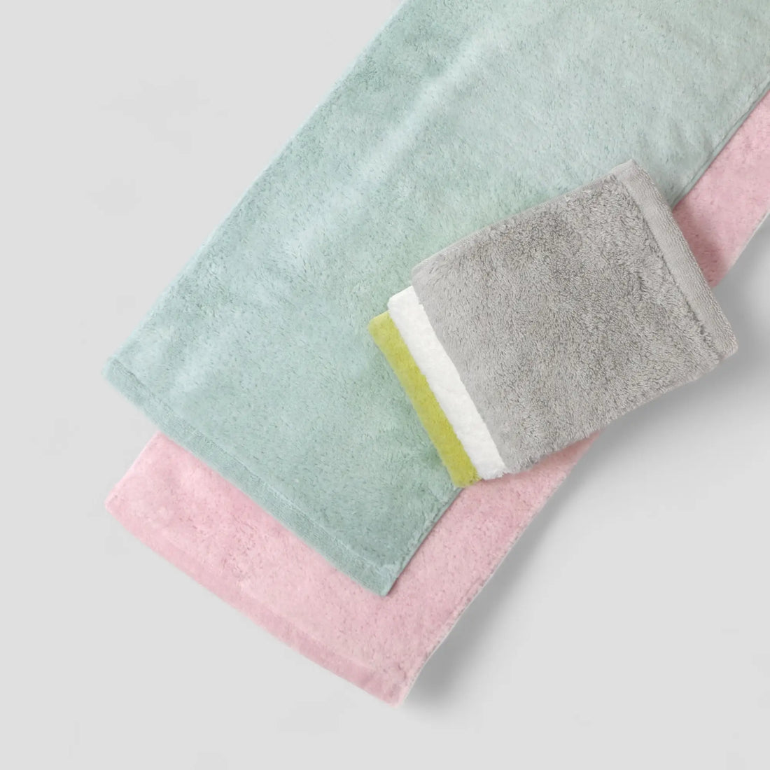 Set of three folded Imabari towels in green, gray, white, blue and pink on a light gray background