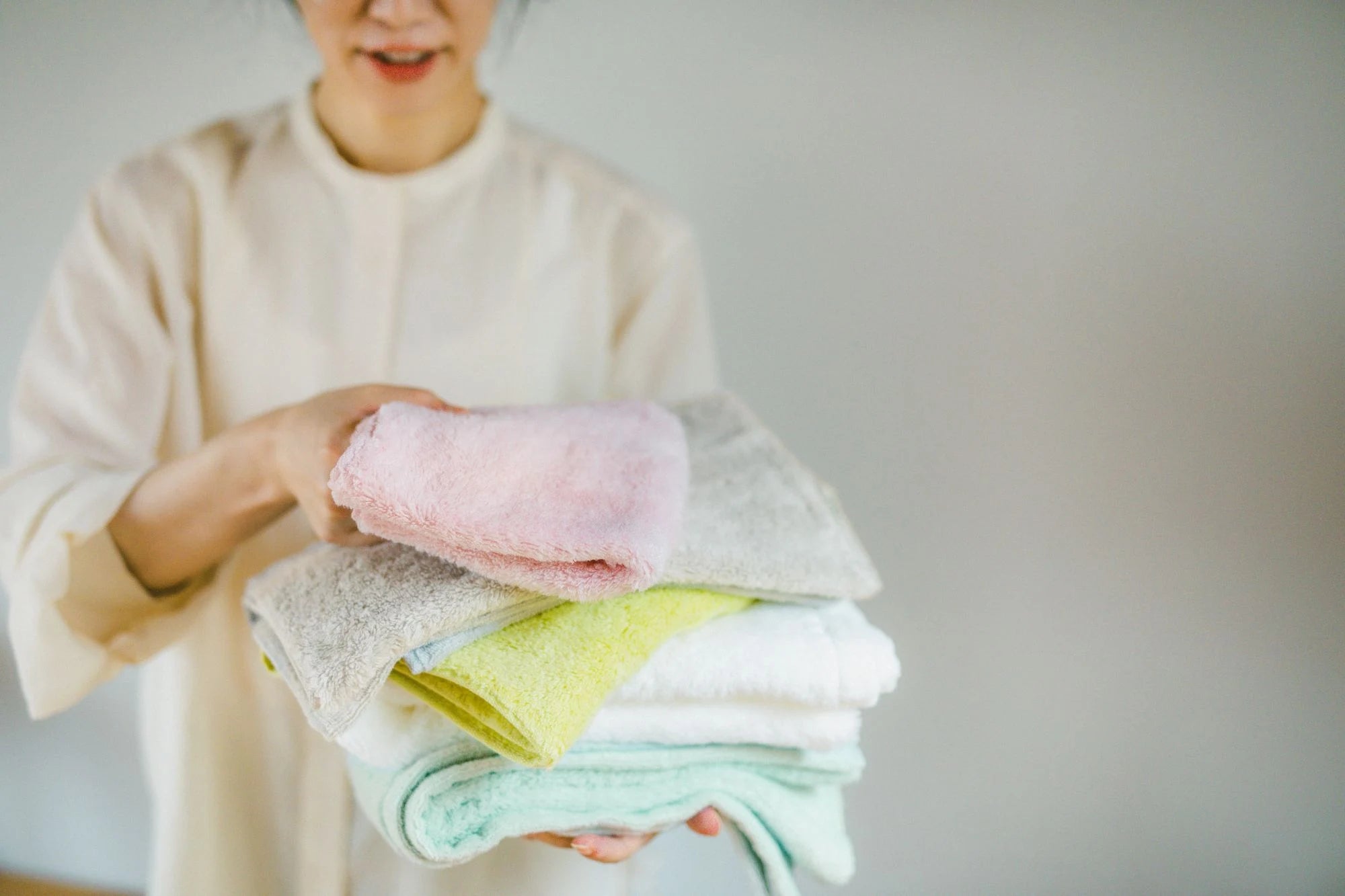 Person holding a stack of folded colorful Imabari towels against a neutral background
