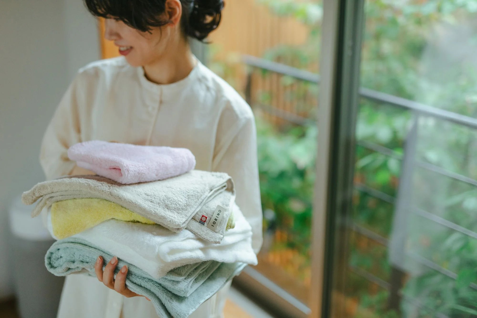 Person holding folded Imabari towels in a home setting with greenery outside