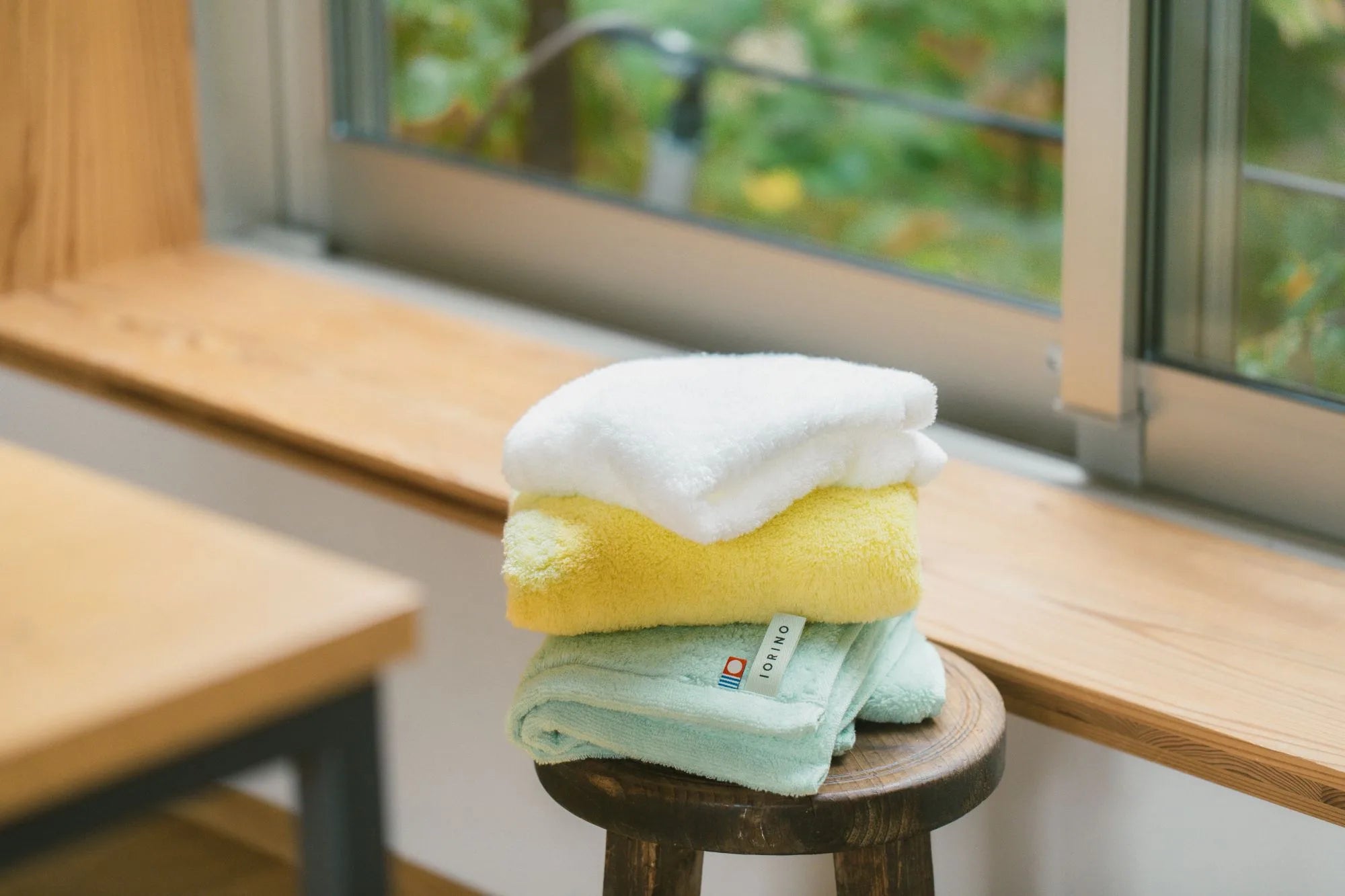 Stack of folded Imabari towels on a wooden stool with a blurred outdoor background