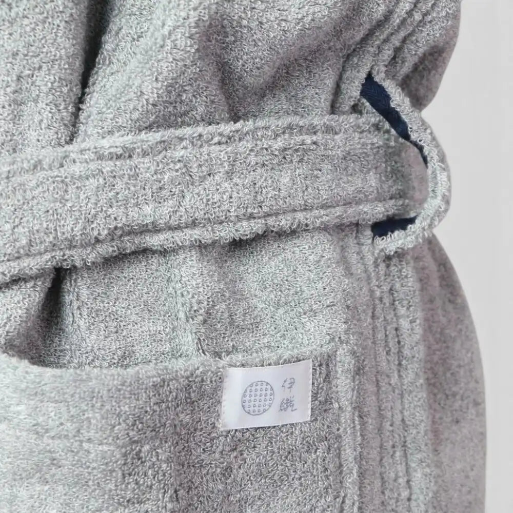 Close-up of a gray terry cloth Imabari towel bathrobe with a matching belt and a small white fabric label sewn onto the front pocket.
