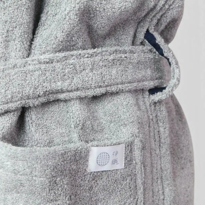 Close-up of a gray terry cloth Imabari towel bathrobe with a matching belt and a small white fabric label sewn onto the front pocket.