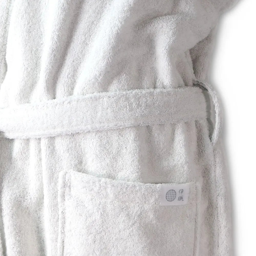 Close-up of a white terry cloth Imabari towel bathrobe with a matching belt and a front pocket, shown against a plain white background.