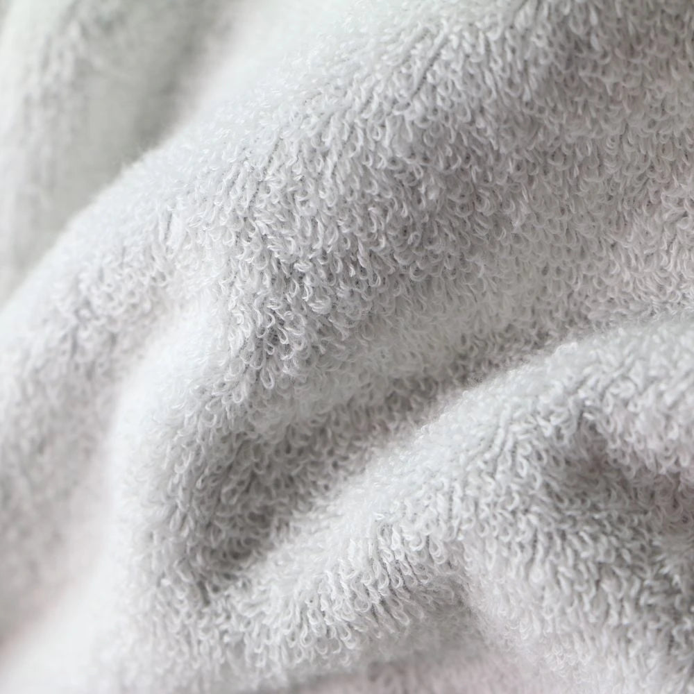 A close-up of a soft, plush terry cloth fabric in a very light gray or off-white color Imabari towel bathrobe, showing the textured loop pile and gentle folds.