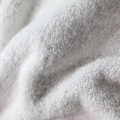 A close-up of a soft, plush terry cloth fabric in a very light gray or off-white color Imabari towel bathrobe, showing the textured loop pile and gentle folds.
