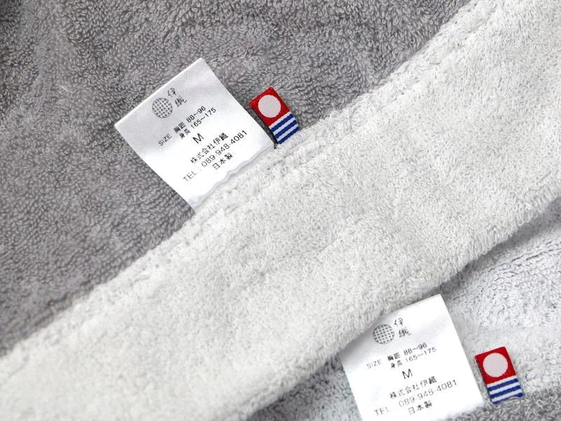 Close-up of a gray plush Imabari towel bathrobe with a white border and sewn-in size labels, showing the fabric texture and Japanese text on the tags.