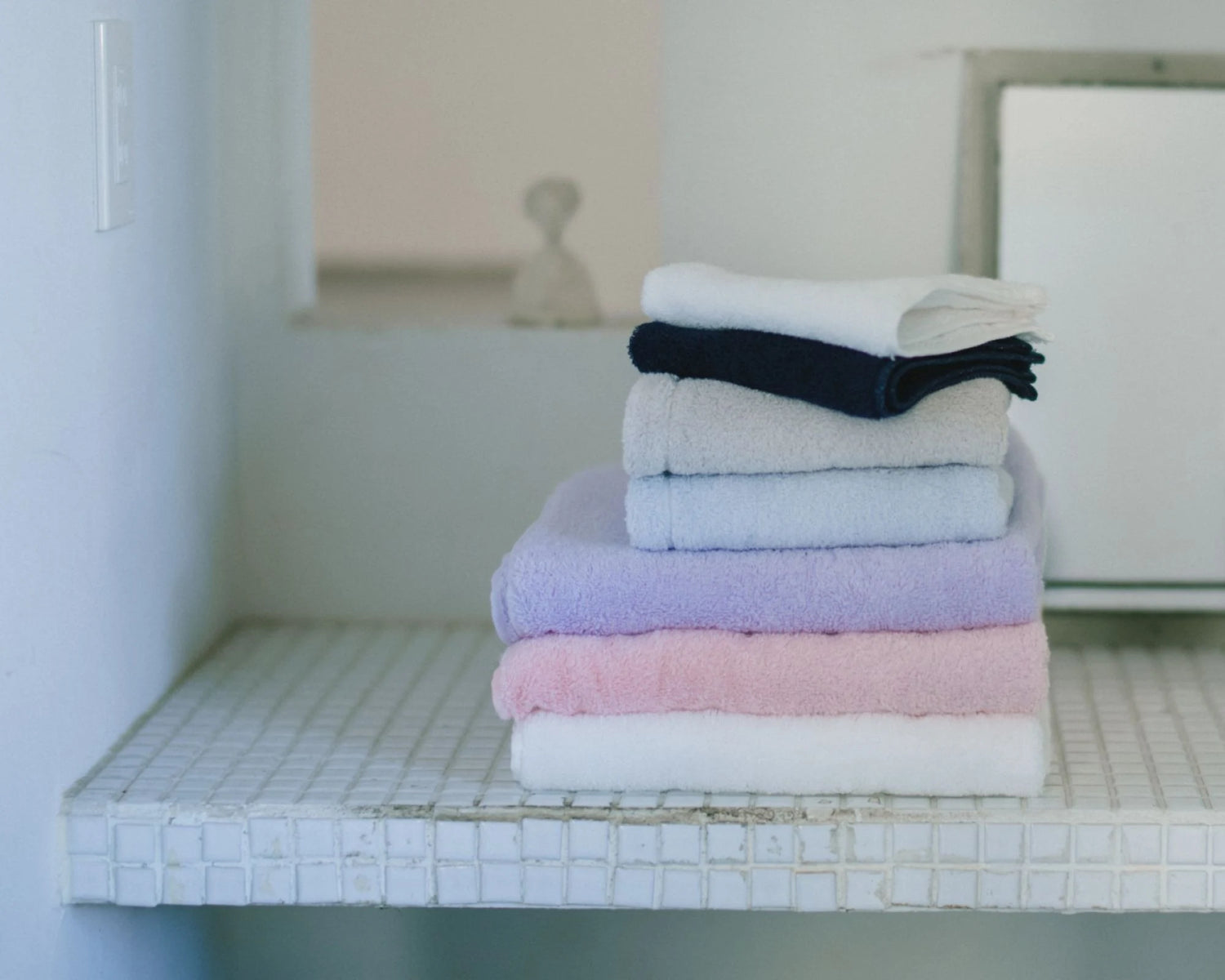 Stack of folded Imabari towels in various colors on a tiled shelf.