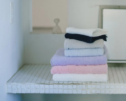 Stack of folded Imabari towels in various colors on a tiled shelf.