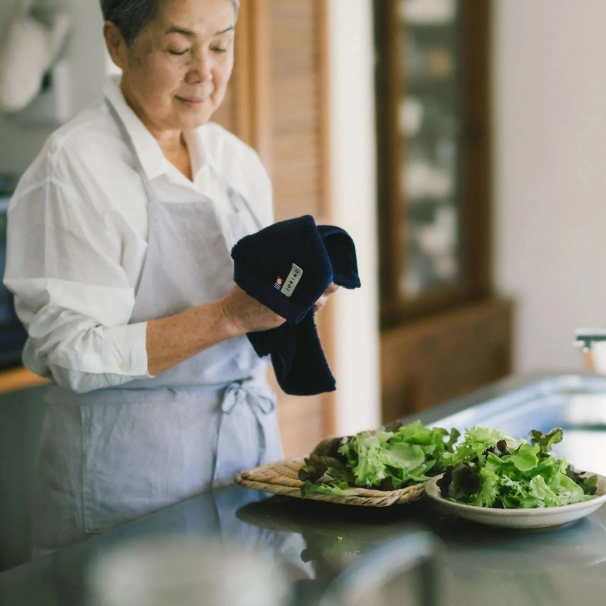 Person in a kitchen holding a navy Imabari towel with salad on a table