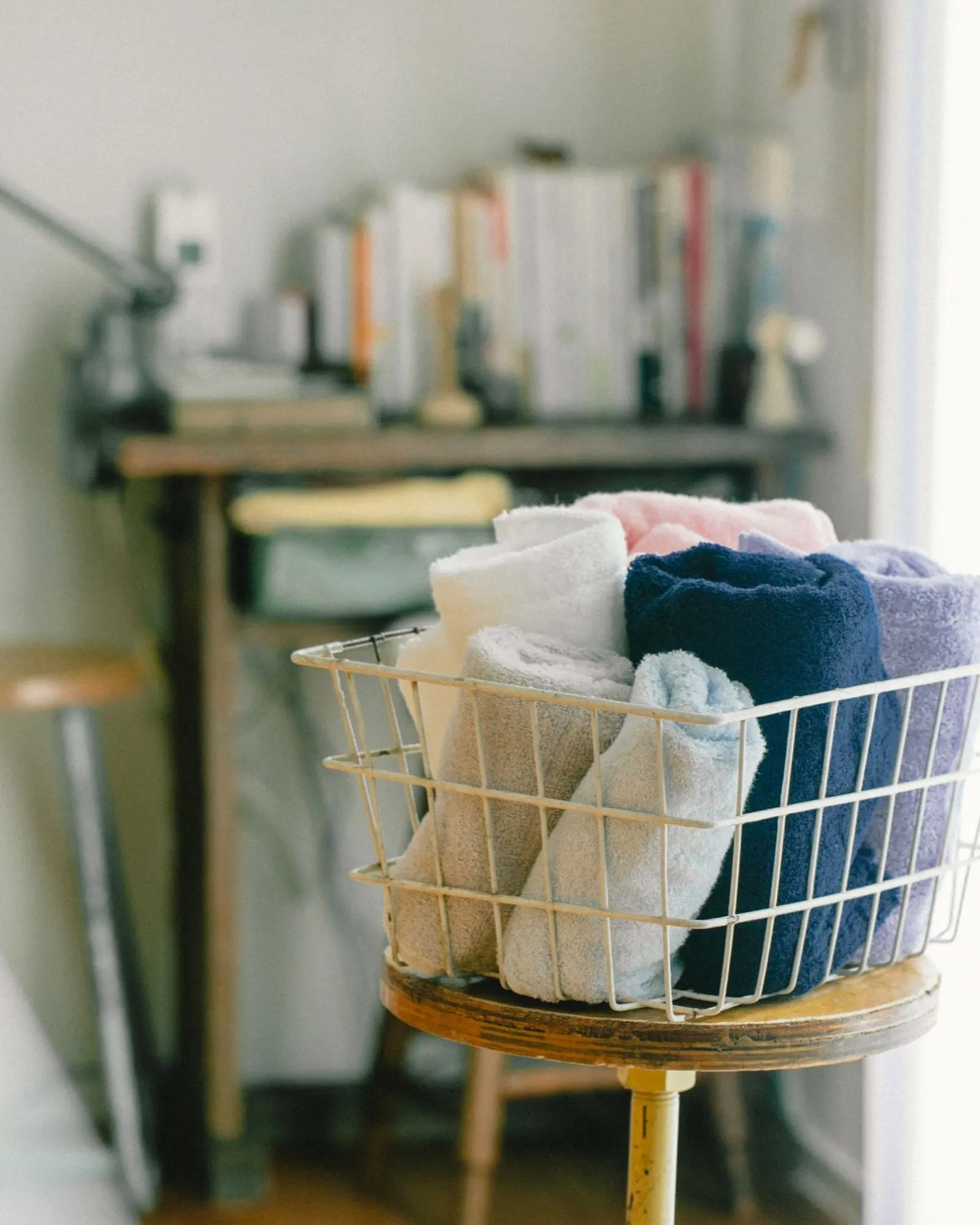 Wire basket filled with folded Imabari towels on a wooden stool in a room setting.