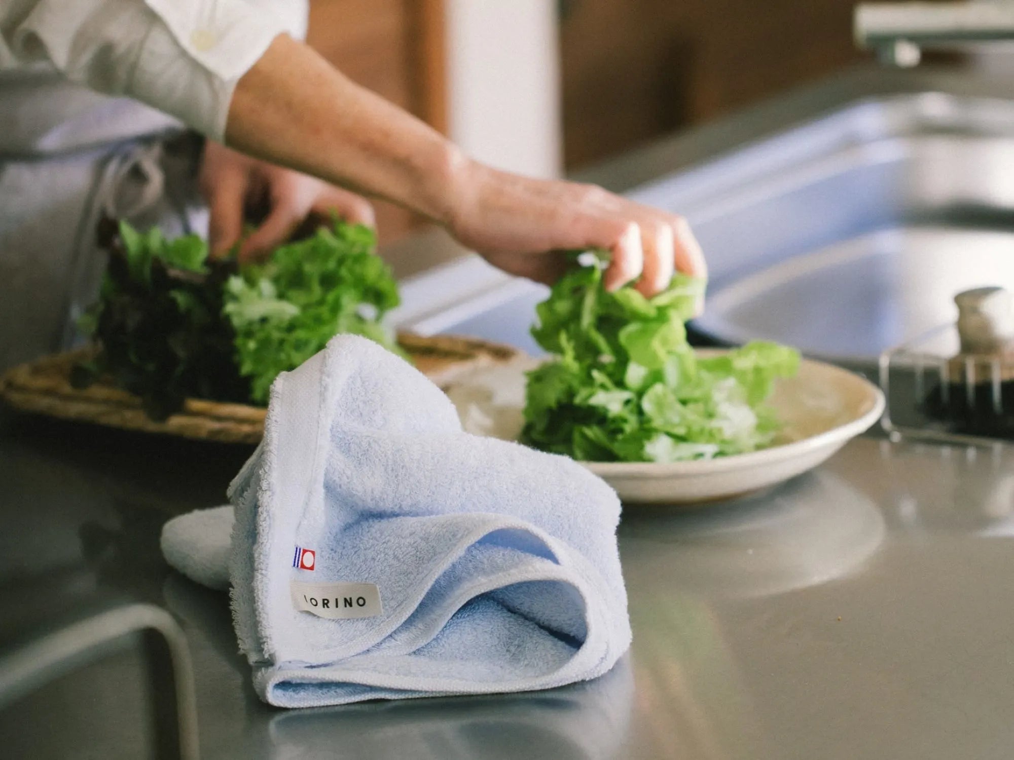 Person preparing food in a kitchen with a blue Imabari towel on the counter