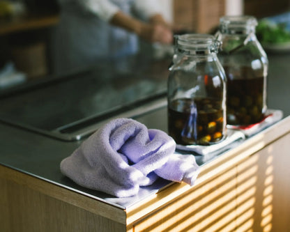 Two glass jars with a dark liquid on a kitchen counter with a purple Imabari towel.