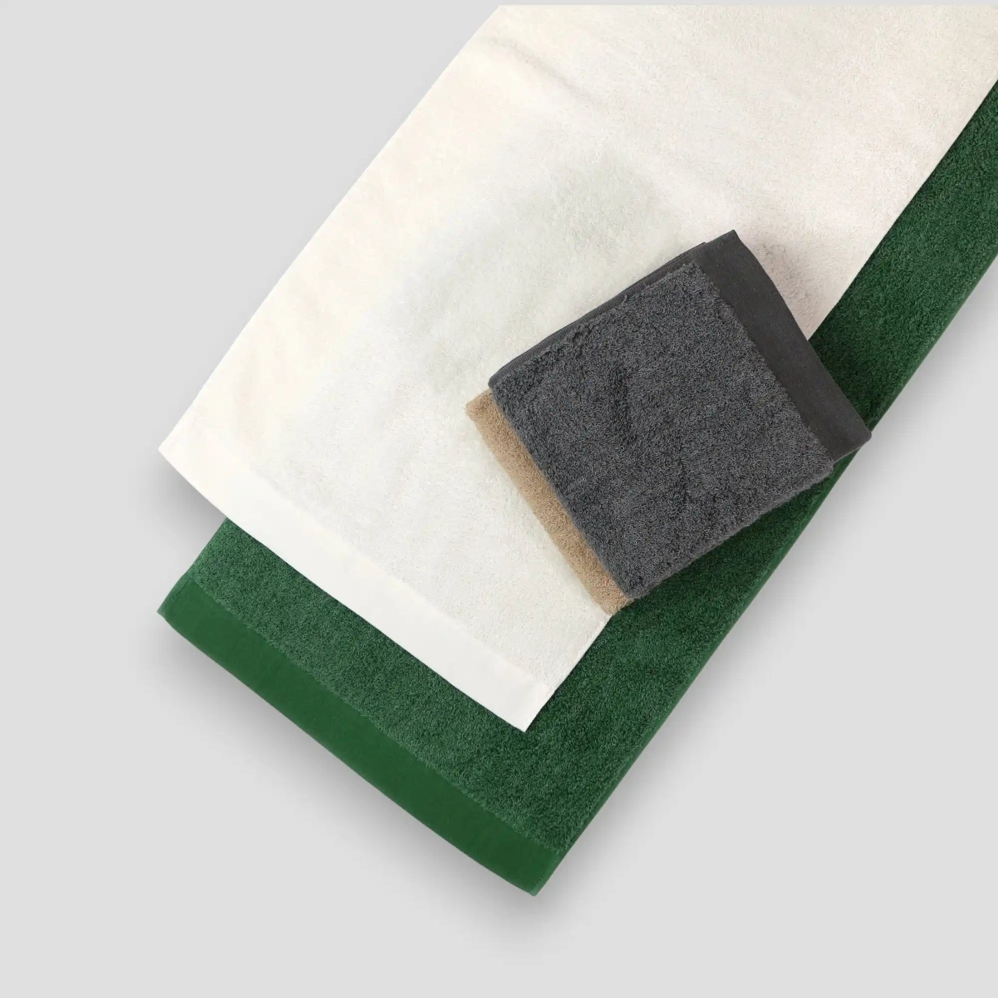 Three folded Imabari towels in white, gray, and green on a light gray background