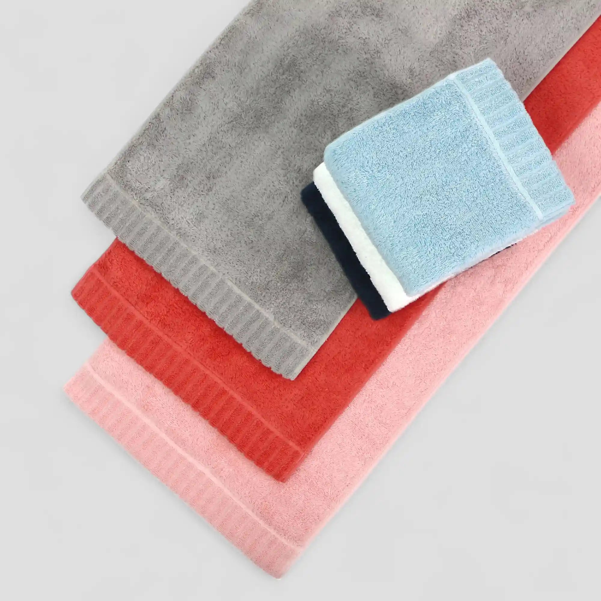 Stack of folded Imabari towels in gray, red, pink, and blue on a light gray background