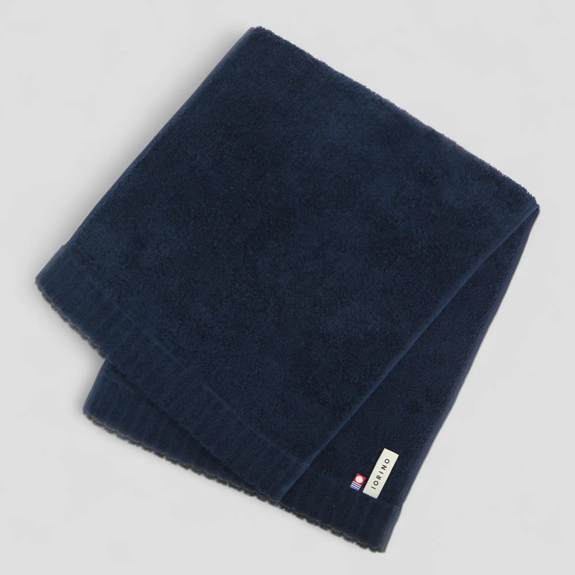 Folded navy blue Imabari towel with a brand label on a light gray background