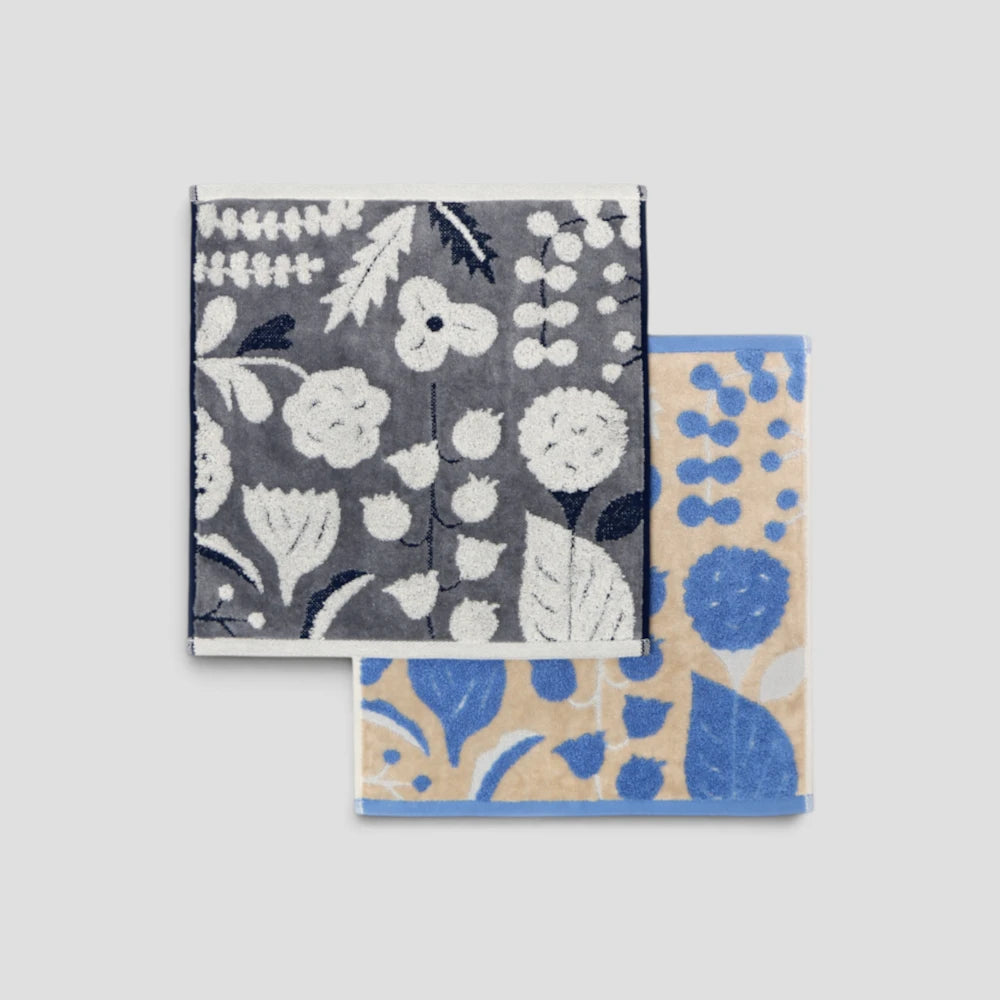 Two square patterned fabric Imabari towel on a light gray background. The top napkin has a dark gray base with white floral and botanical motifs
