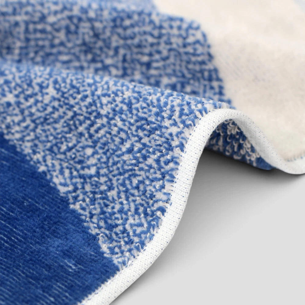 Close-up of a plush area Imabari towel with a textured blue and white pattern and a cream-colored underside, folded over to show the backing and white edge trim.