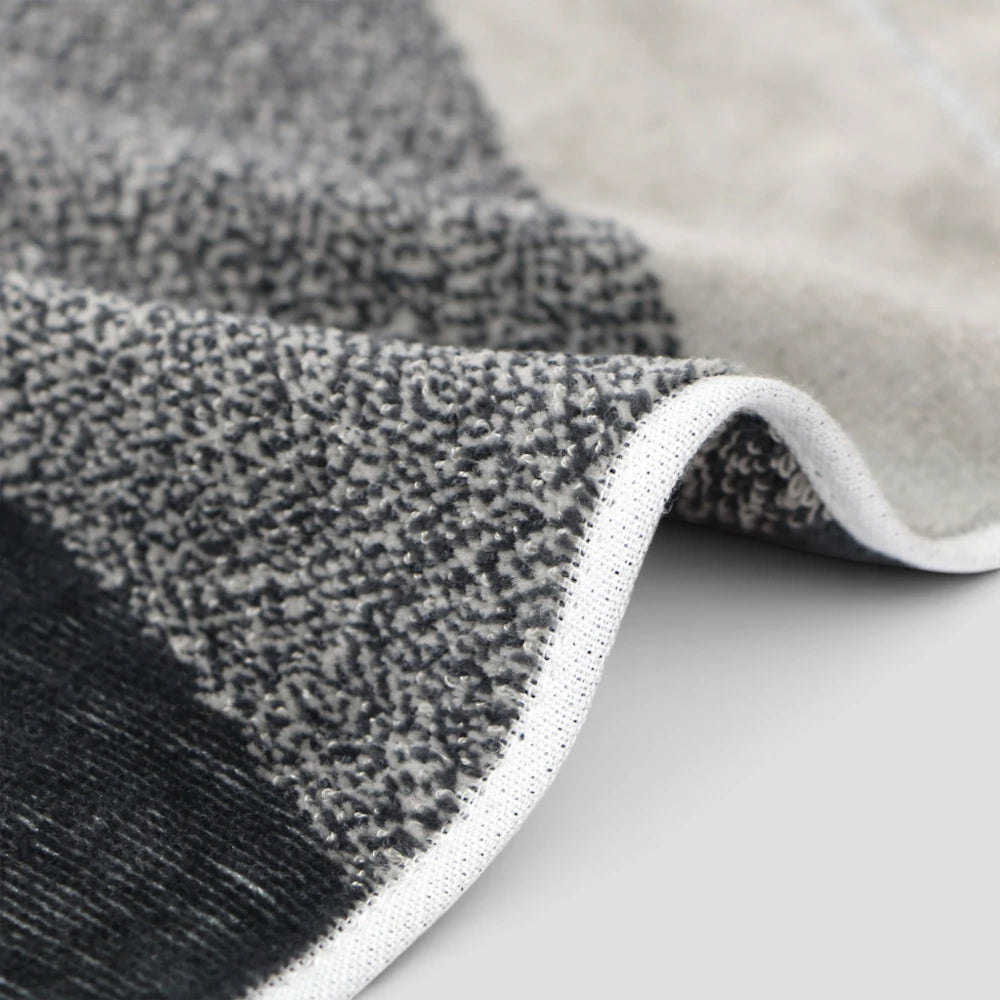 Close-up of a textured Imabari towel with a modern geometric pattern in black, gray, and beige, showing the woven pile and white edge trim.