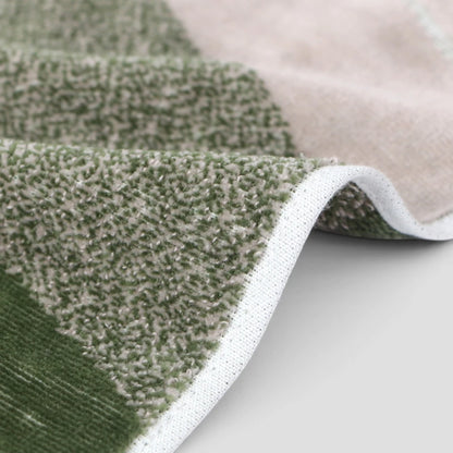 A close-up of a textured Imabari towel with a green and beige striped pattern, folded to show its plush looped texture and white stitched edge.
